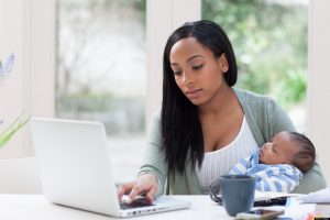 Mother holding baby son and using laptop